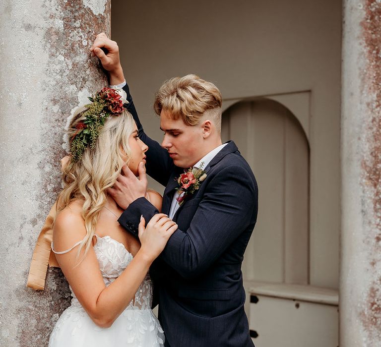 Boho bride wearing flower crown in bespoke wedding dress with groom in blue suit 