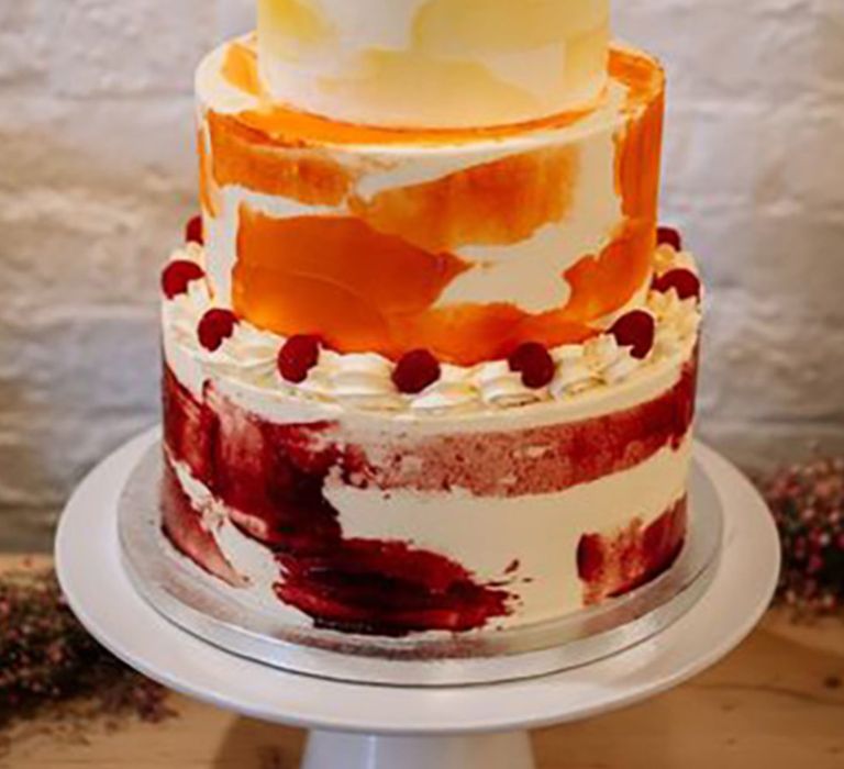 Ombre decorated wedding cake with three tiers decorated in white icing with red, orange and yellow paint designs 