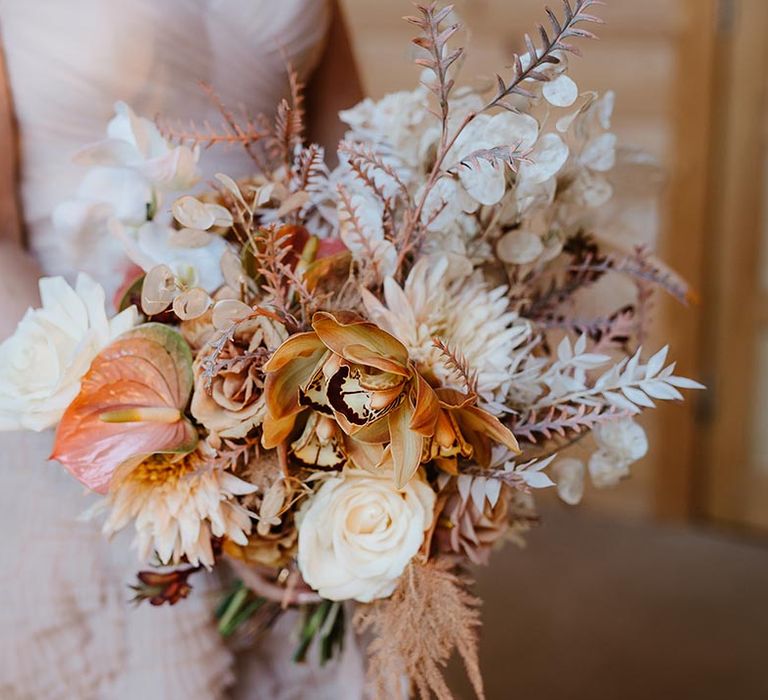 Bride carrying neutral tone wedding bouquet with roses, anthuriums and leaves for boho wedding 