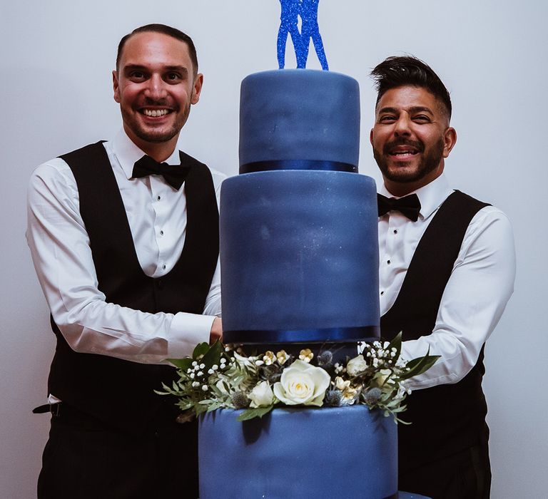 Two grooms cut their navy blue wedding cake at their gay wedding 