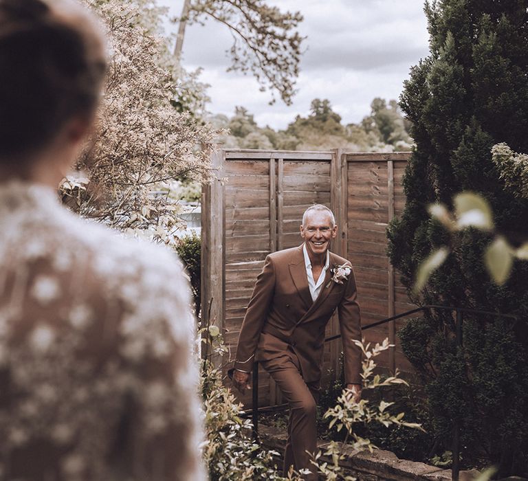 Father of the bride in chocolate suit has first look at bride in her wedding dress 