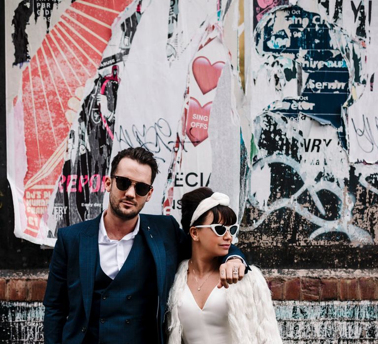 Bride in trouser suit and sunglasses and groom in navy suit and Ray Bans 