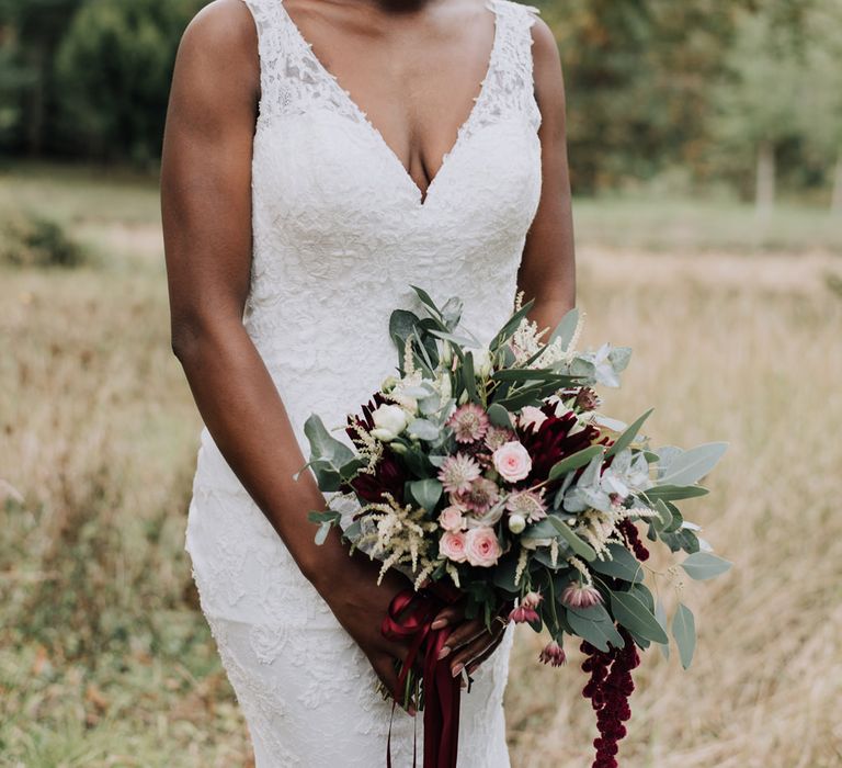 Bride in lace wedding dress with straps and burgundy wedding bouquet 