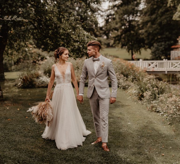 Bride and groom holding hands in garden with pampas grass bouquet 