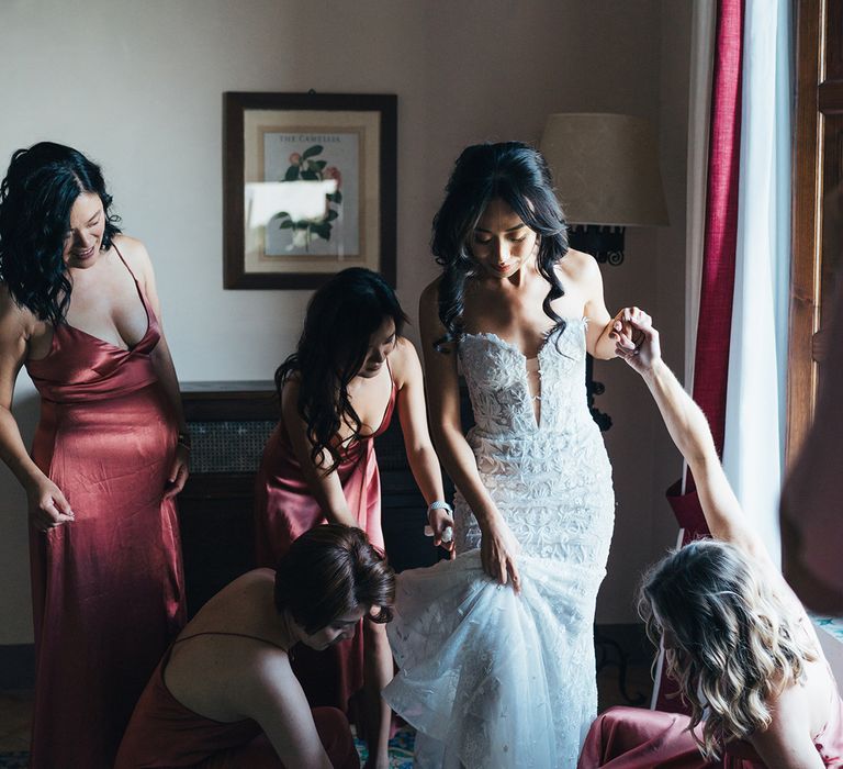 Bridesmaids helping the bride put on her bridal gown on the wedding morning 