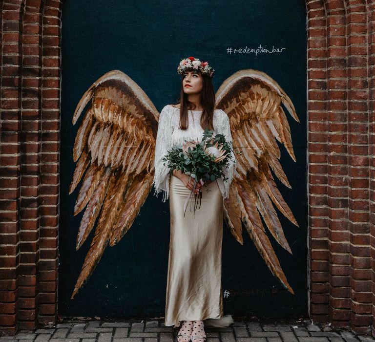 Bride poses against graffiti of angel wings holding bouquet