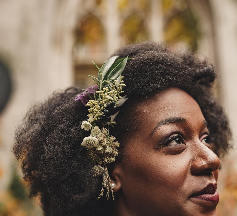 Wedding hairstyles for Black brides. A Bride wears real flowers in the side parting of her afro as she smiles off camera