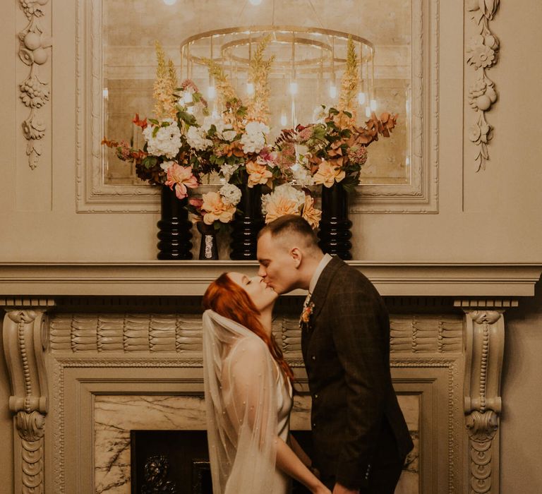 Bride and groom kissing at Old Marylebone Town hall in front of a beautiful wedding flower installation 