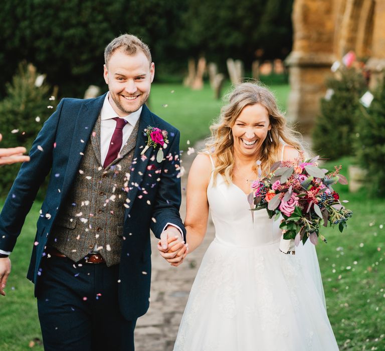 Bride & groom walk through confetti whilst holding hands