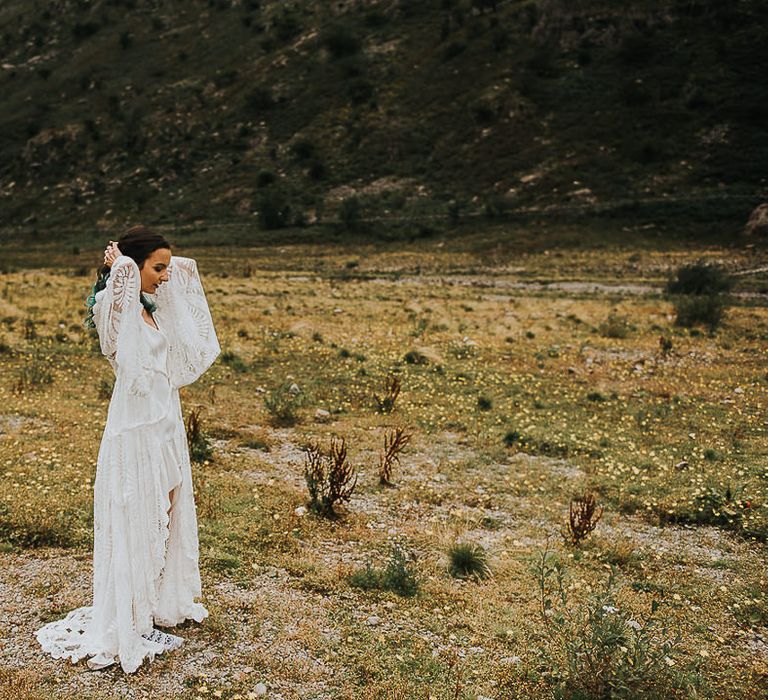 Bride walks through the countryside wearing bell sleeved lace wedding gown