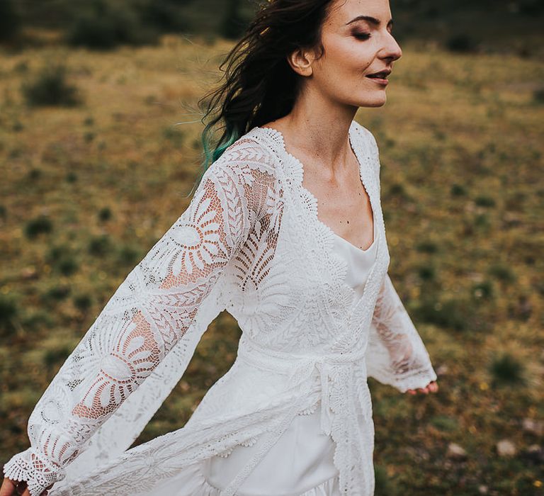 Bride walks through the countryside with eyes closed wearing bell sleeved wedding gown