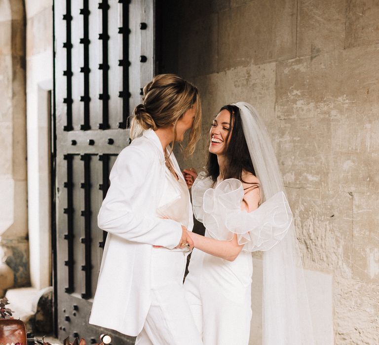 Beautiful same sex couple in off the shoulder jumpsuit with ruffle detail and white trousers suit 