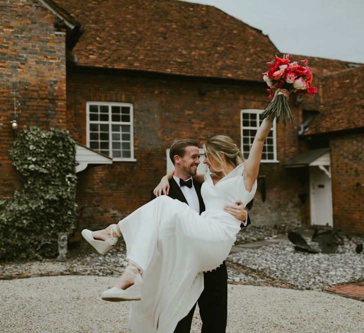 Bride lifts bouquet above her head as groom picks her up