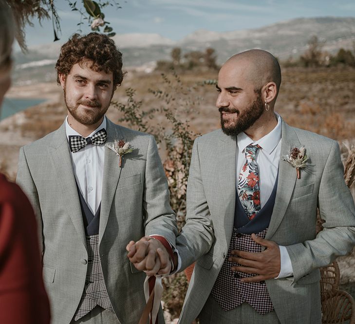 A gay couple marry in hand fasting ceremony on the beach. they wear matching grey suits.