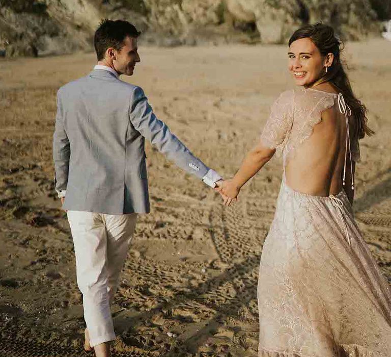 Groom leads bride down the beach in Cornwall