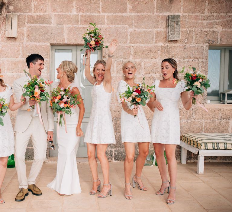 The bride and her bridal party, all wearing white and carrying orange flower bouquets