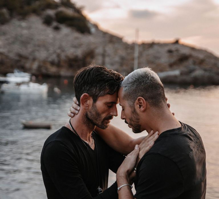 Grooms look tenderly at one another as the sun sets in the background 