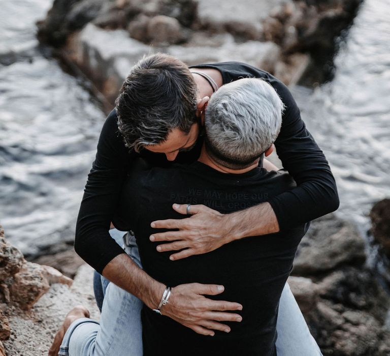 Grooms hug beside the sea in Ibiza during engagement session