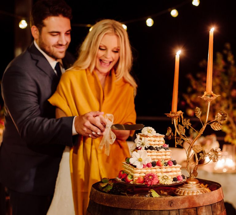 The bride and groom cutting into their pastry and meringue wedding cake decorated with flowers