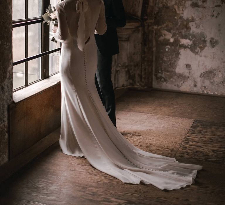 Bride & groom stand beside window together whilst looking at one another