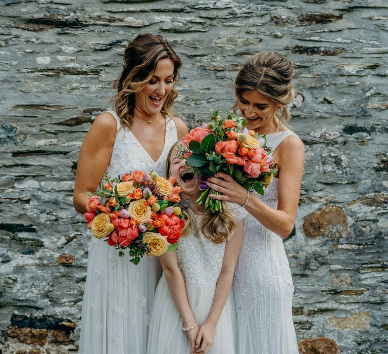 Brides stand with their daughter and bridesmaid whilst holding bright floral bouquets