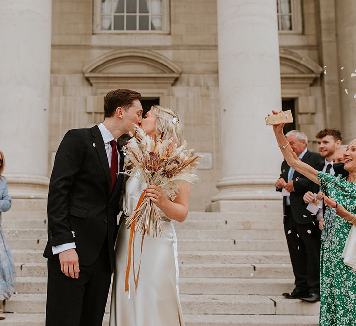 Bride holding a dried flower bouquet during the confetti moment outside of Leeds Civic Hall