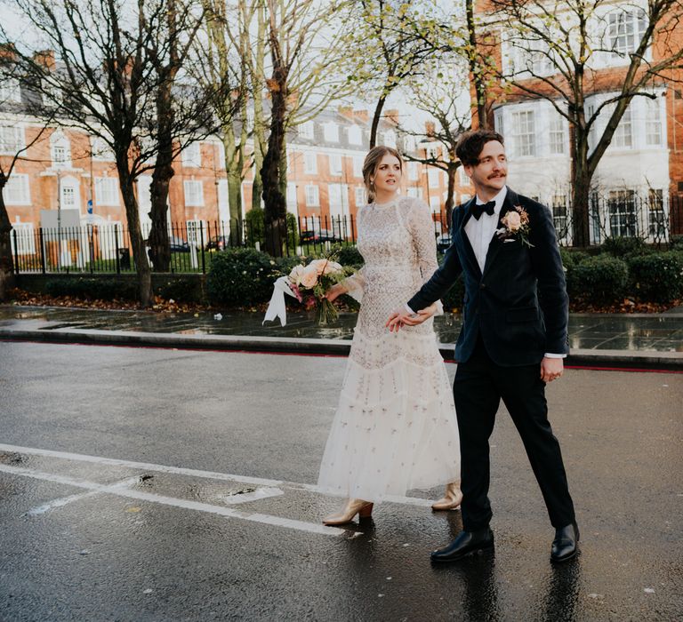 Bride & groom walk hand in hand with one another as they cross the street together