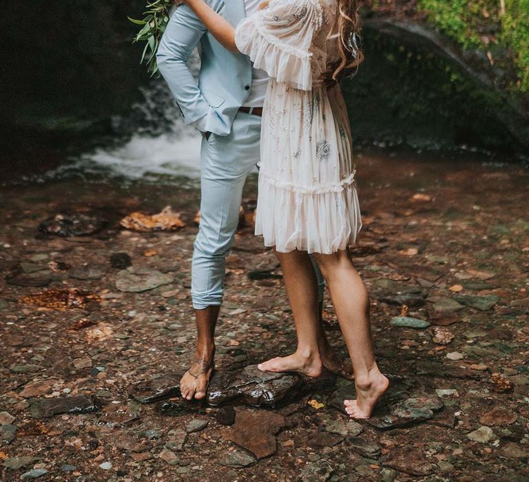 Bride & groom kiss outdoors in front of waterfall on their wedding day