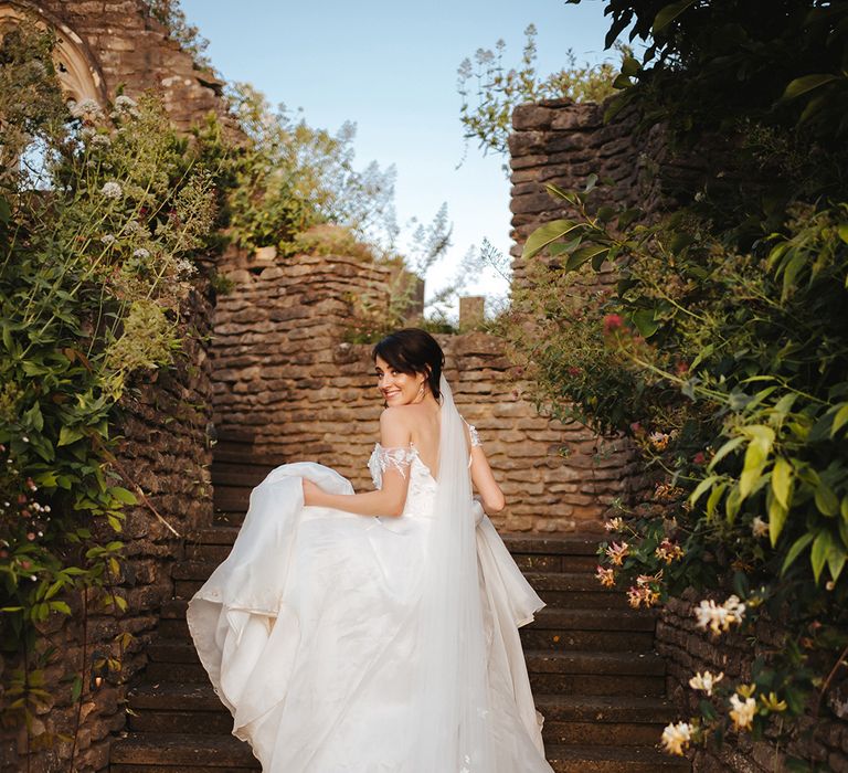 Bride walks up staircase whilst holding her gown on her wedding day