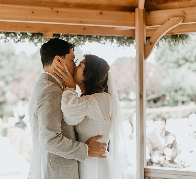 Bride & groom kiss on their wedding day outdoors for Secret Garden wedding