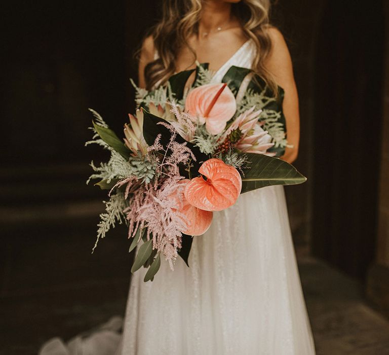 Bride holds tropical bouquet complete with palm leaves and peach anthurium