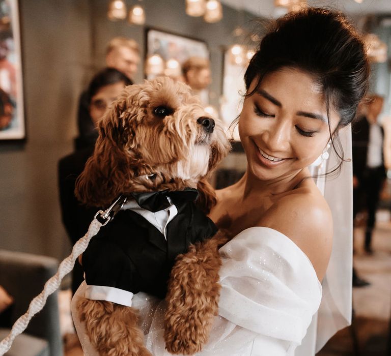 East Asian bride in a strapless wedding dress holding her golden cockapoo pet in a tuxedo at her pub reception 