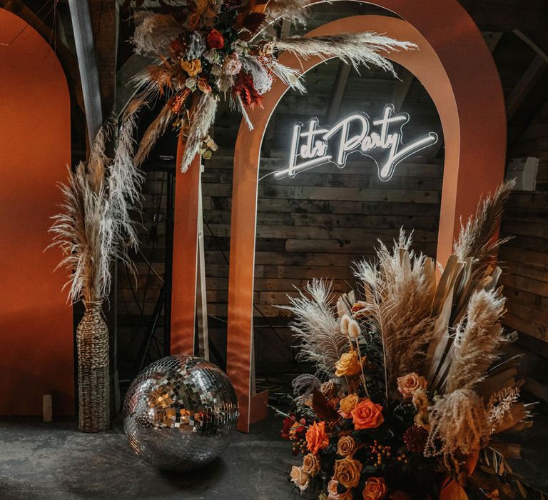 Orange wedding decor with arches, neon lights, flower clouds and disco balls for boho wedding