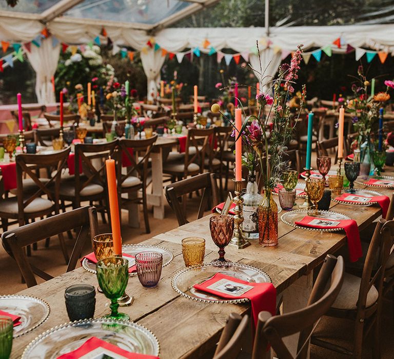 Vibrant wedding table decor with coloured goblets, napkins, flowers and candles in a clear marquee 