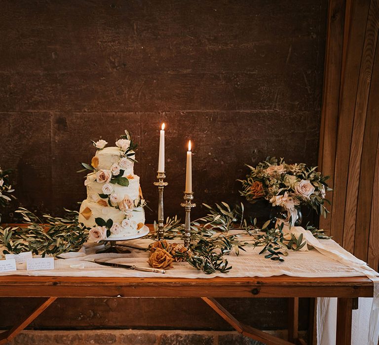 Buttercream wedding cake decorated with flowers on a cake table with candlesticks and floral arrangements 