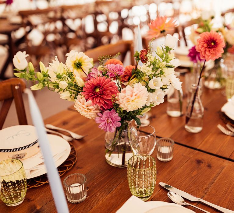 Bright florals in glass vases in wooden tables with tambourine wedding table place names for rustic garden wedding reception