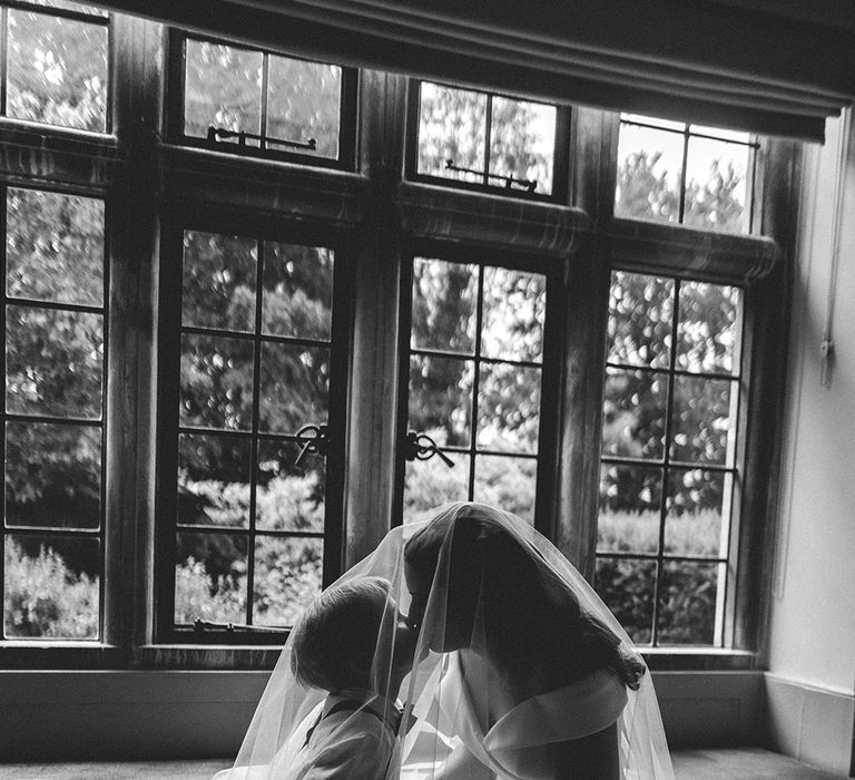 Bride in an off the shoulder Suzanne Neville wedding dress kissing her son under her wedding veil on the wedding morning 