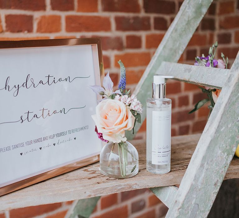 Hydration station sign in rose gold frame with flower details and hand sanitiser