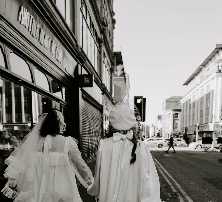 Manchester elopement with two brides in short wedding dresses with a long veil and berret hat holding hands 