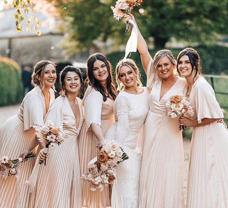 Bride in beaded long sleeve wedding dress with bridesmaids in pale pink butterfly sleeve pleated v-neck dresses and neutral bouquets