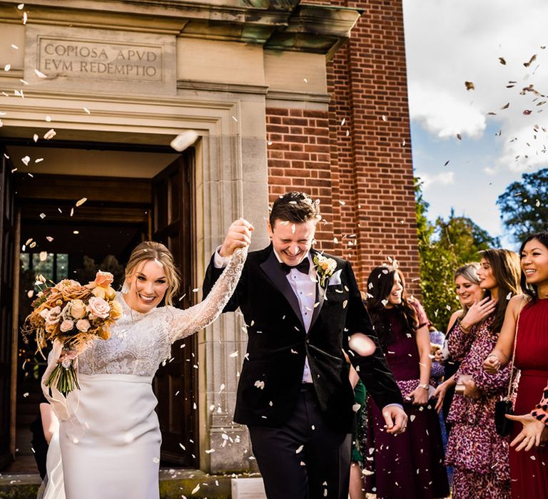 Bride in lace top long sleeve wedding dress holding neutral bouquet and groom in black tie exit their ceremony