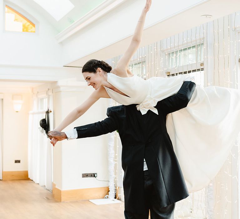 Groom lifts the bride in an airplane lift she wears a halter neck pleated gown from Jesus Peiro