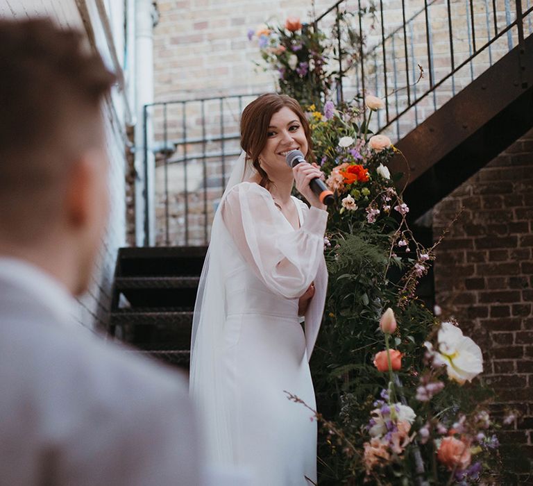 Bride in Suzanne Neville wedding dress with custom sheer puff sleeves giver a bride speech at the wedding 