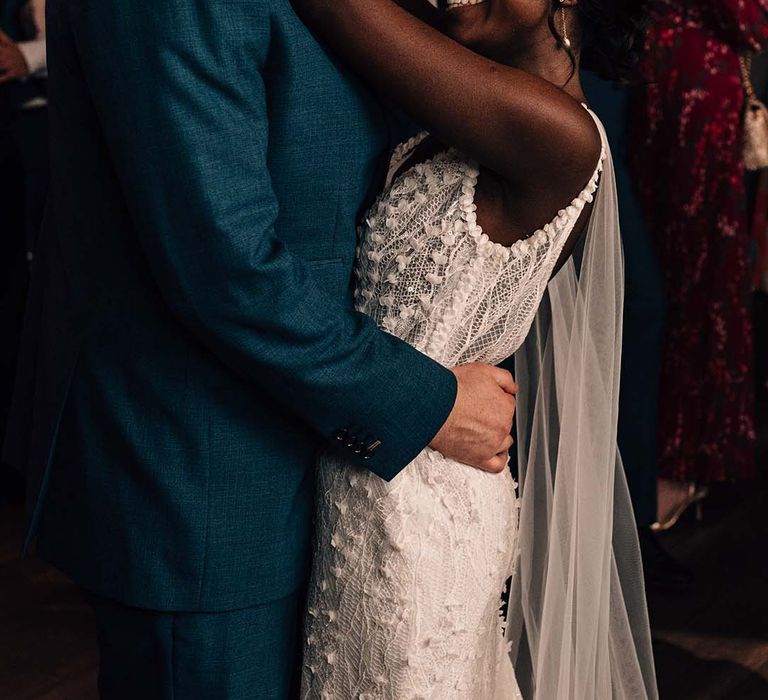 Bride in lace detail dress and groom in dark blue suit engaging in their first dance