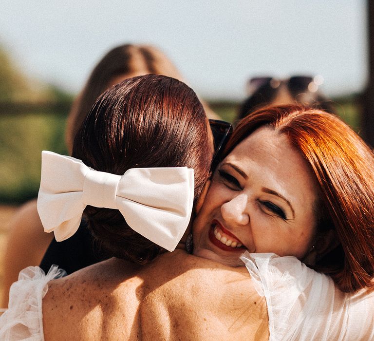 Bride with red hair and large hair bow accessory hugs a wedding guest 