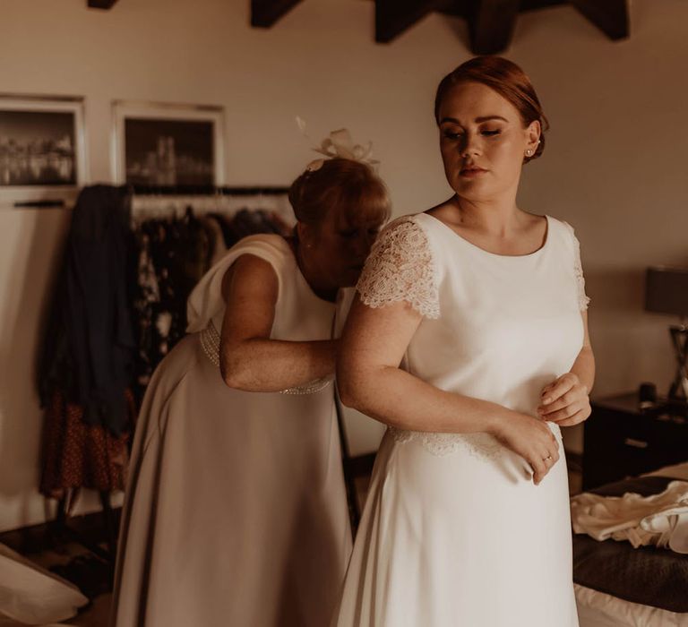 Bride wears round neck wedding gown complete with lace sleeves and her red hair in chignon bun 