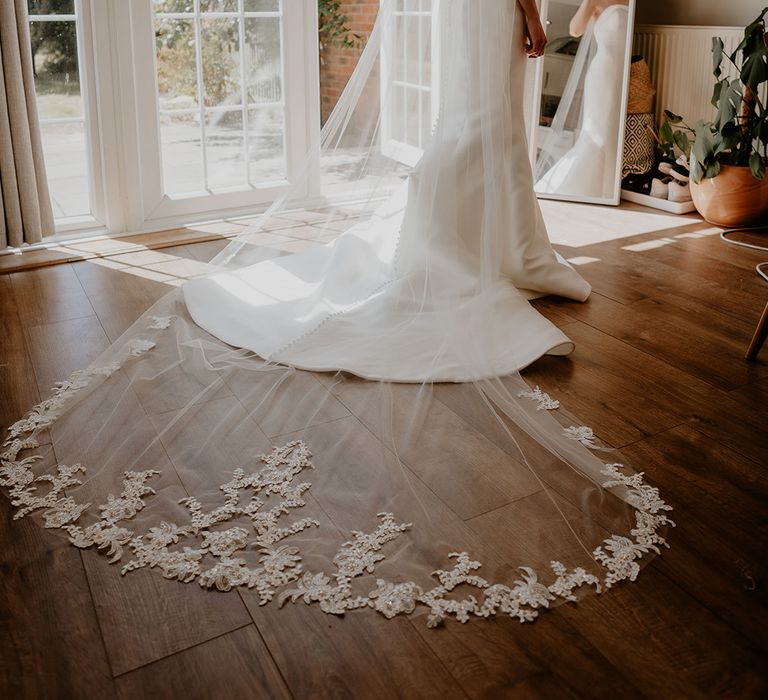 Bride in strapless button back wedding dress with a long veil with an embroidered edge 