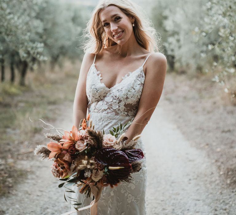 Bride wears Emmy Mae Bridal lace wedding dress whilst holding bouquet filled with orange orchids, deep red anthurium and bunny ears 