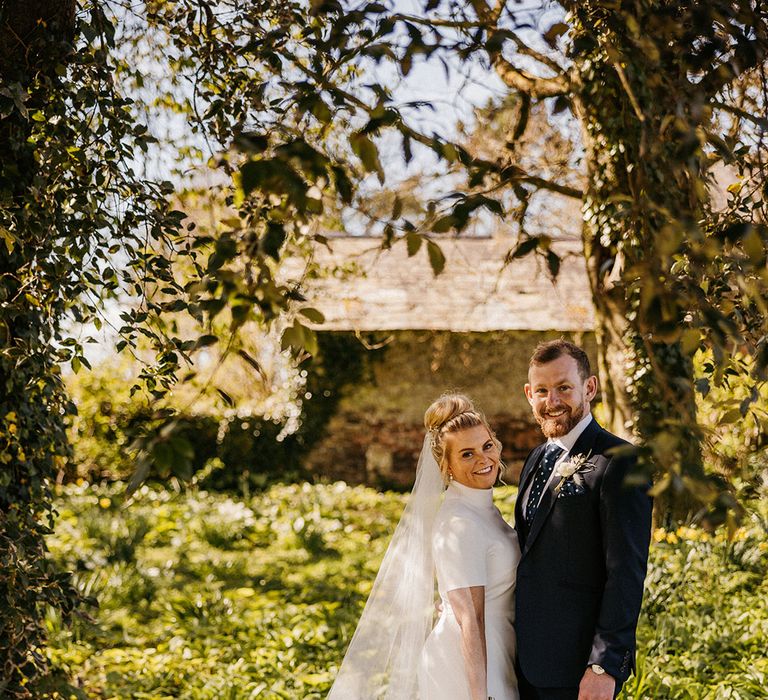 Groom in a blue suit with a Polks dot tie and handkerchief with bride in a pearl wedding veil and high neck wedding dress from Jesus Peiro