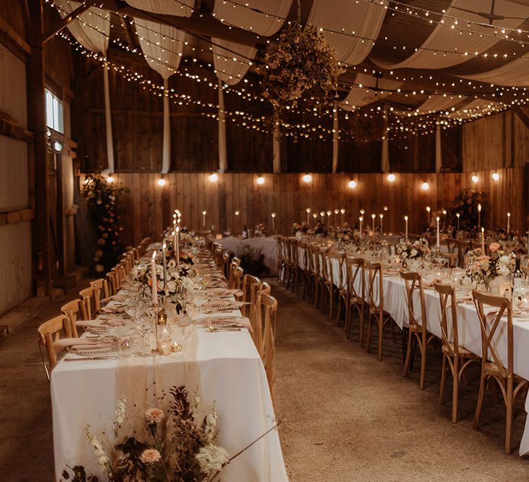 Soft and romantic barn wedding reception with candles and fairy lights with wedding drapes with a blush pink and muted tone tablescape